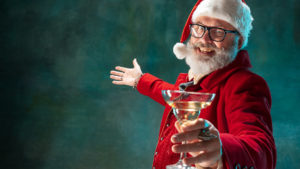A smiling Santa holding a martini wearing a red suit and celebrating at a holiday work party.