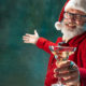 A smiling Santa holding a martini wearing a red suit and celebrating at a holiday work party.