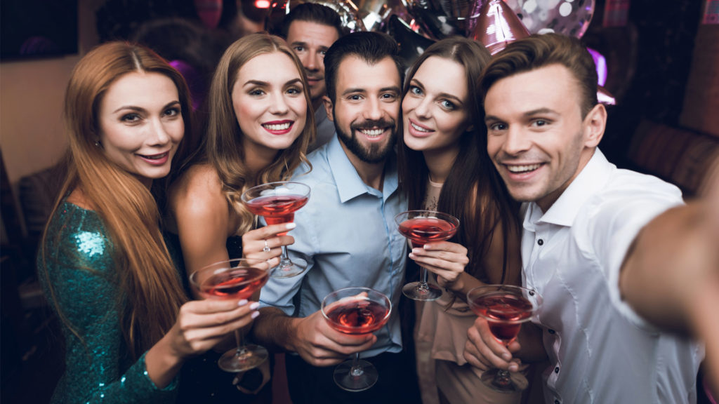 A group of friends with cocktails taking a selfie at a post pandemic party.