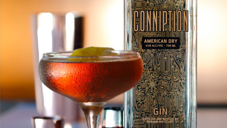 A gin cocktail with a lemon twist next to a bottle of Conniption American Dry gin